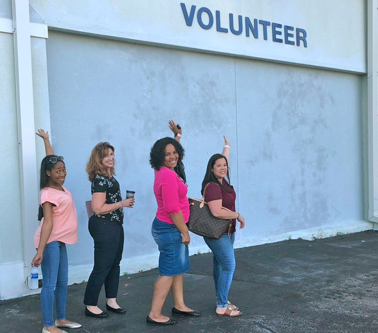 four women pointing to volunteer sign